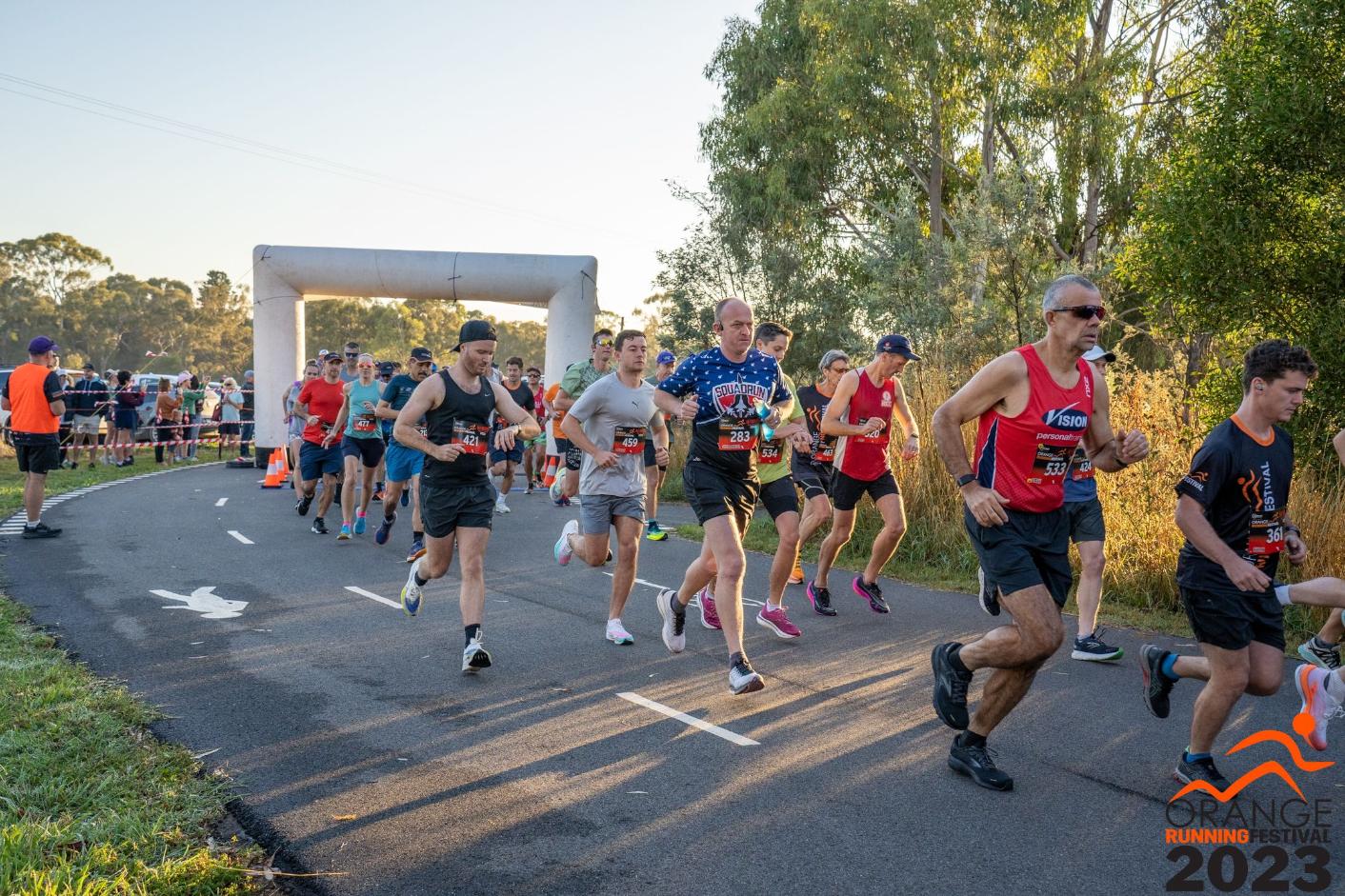 Group of people running on a path away from a starting arch.